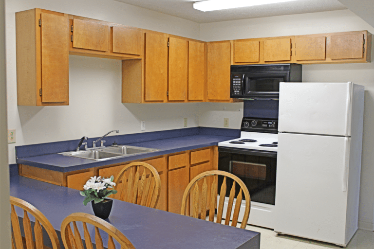 The kitchen inside of on apartment in Young Hall. There is a refrigerator, stove, microwave, sink, and table.