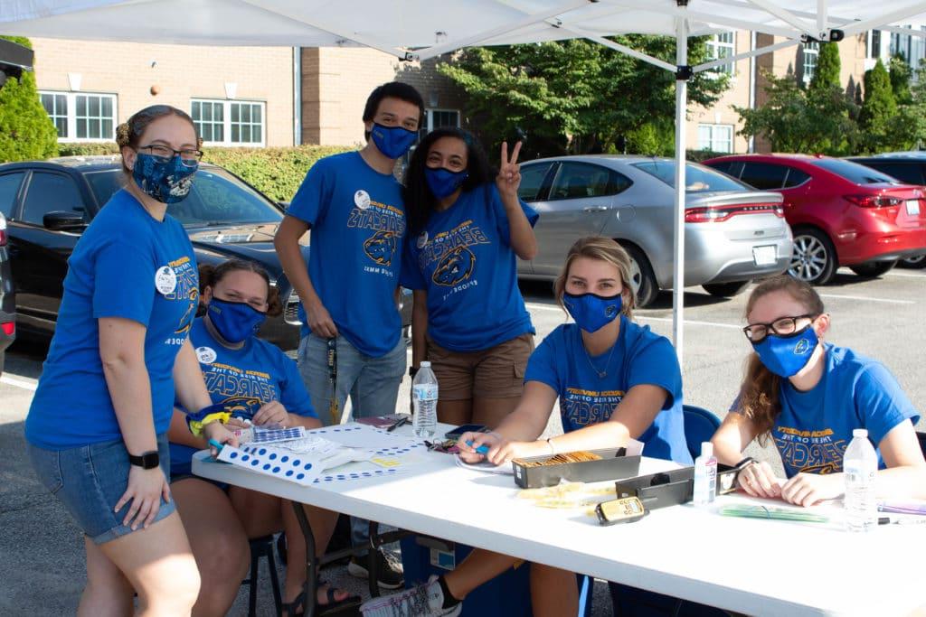 Group of students, wearing blue masks and matching blue shirts, are at a table outside for Orientation